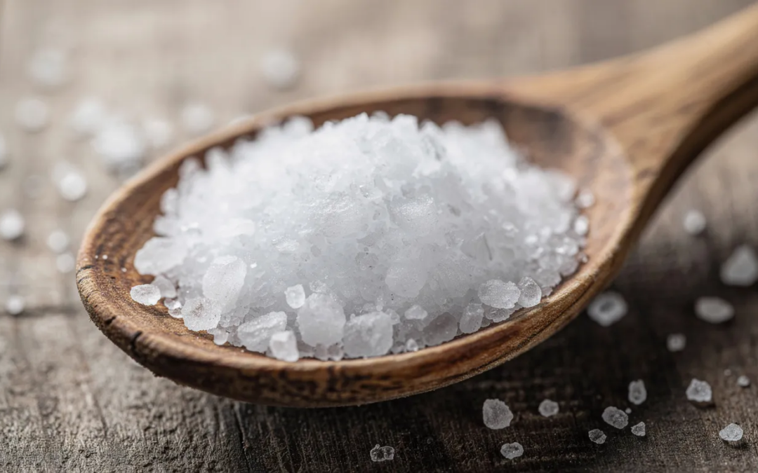 Auf einem Holzlöffel liegen glitzernde weiße Salzkristalle, die als Kochsalz bekannt sind. Diese Salzkristalle sind ein wichtiger Bestandteil der Ernährung und spielen eine bedeutende Rolle für die Gesundheit, insbesondere in Bezug auf den Natrium- und Chloridgehalt, der Einfluss auf Blutdruck und Herz-Kreislauf-Erkrankungen haben kann.